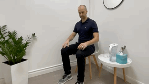 A male massage therapist sitting on a chair and showing how to do soleus raises also know as heel or calves raises